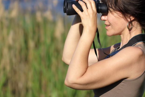 The image shows a woman birdwatching and using binoculars.