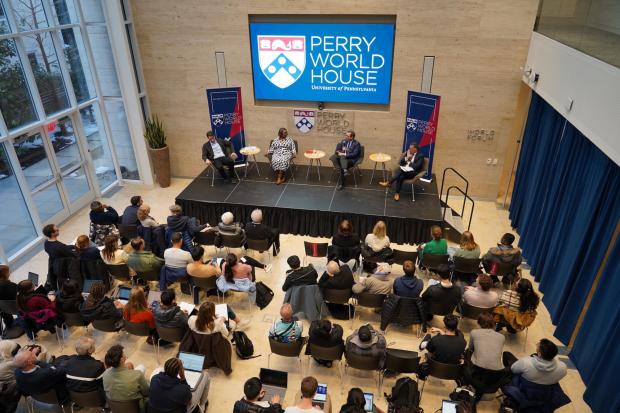 Four speakers sit on a stage in front of a screen reading Perry World House and the Penn shield, in front of a packed audience at Perry World House.