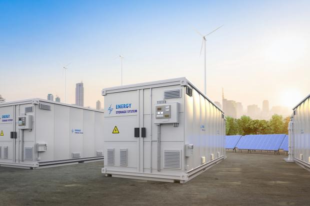 Energy storage systems or battery container units with solar and turbine farms in background.