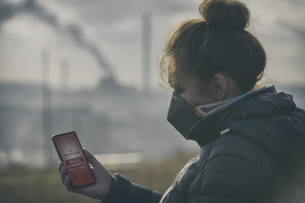 Person holding phone checking air pollution levels outside wearing a mask.