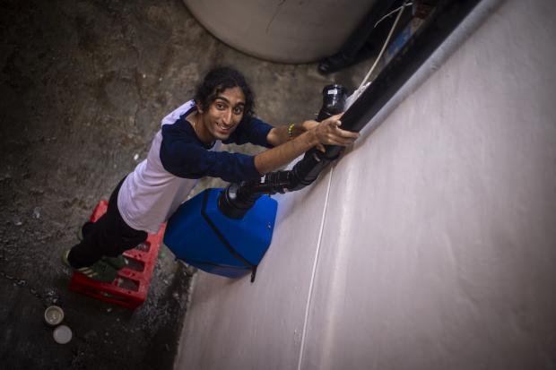 Krishna Chandrasekhara stands on a milk crate, holding plastic water piping for a rooftop water harvesting system in Mexico.