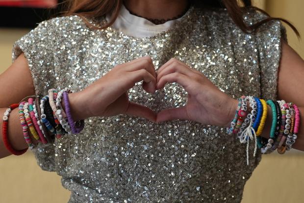 A Taylor Swift fan with friendship bracelets makes a heart sign with their hands.