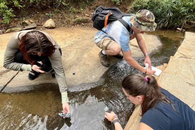 Three people test water below a sand dam.