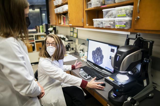 Archaeologist Kathleen Morrison (center) and anthropology doctoral student Moriah McKenna discuss one of the charred lumps from a 2010 excavation in southern India. The image is possible thanks to a new microscope, seen here on the right, that takes and stitches together high-resolution images in incredible detail. (Image: Eric Sucar)